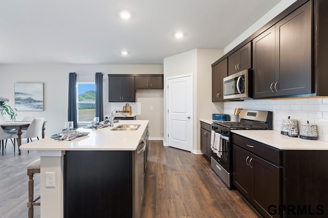 kitchen featuring sink, dark wood-type flooring, appliances with stainless steel finishes, backsplash, and an island with sink