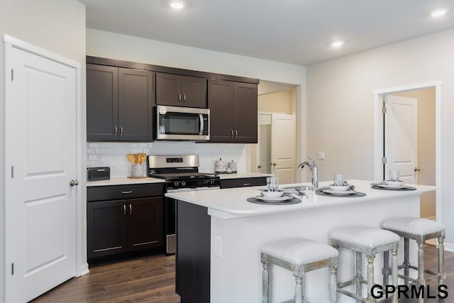 kitchen featuring appliances with stainless steel finishes, a breakfast bar, decorative backsplash, a kitchen island with sink, and dark brown cabinetry