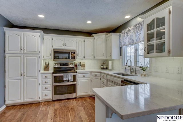 kitchen featuring sink, light hardwood / wood-style flooring, kitchen peninsula, stainless steel appliances, and white cabinets