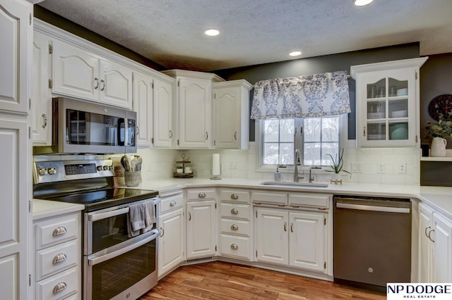 kitchen featuring sink, tasteful backsplash, stainless steel appliances, light hardwood / wood-style floors, and white cabinets