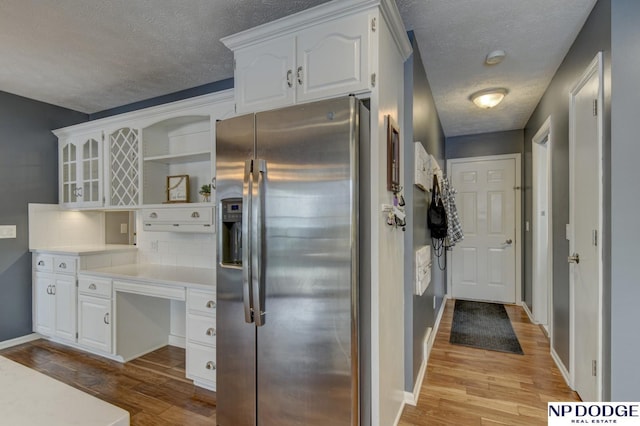 kitchen with white cabinetry, a textured ceiling, stainless steel fridge with ice dispenser, decorative backsplash, and light wood-type flooring