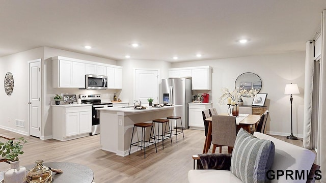 kitchen with appliances with stainless steel finishes, a kitchen island with sink, white cabinetry, a kitchen bar, and light wood-type flooring