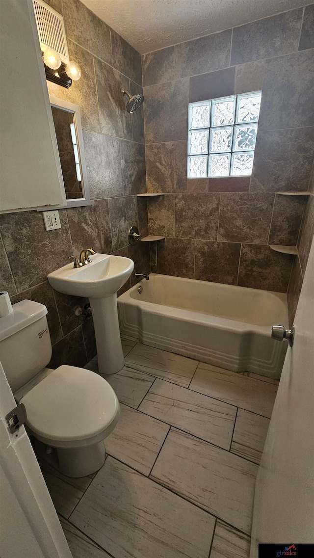 bathroom featuring tiled shower / bath combo, tile walls, and toilet