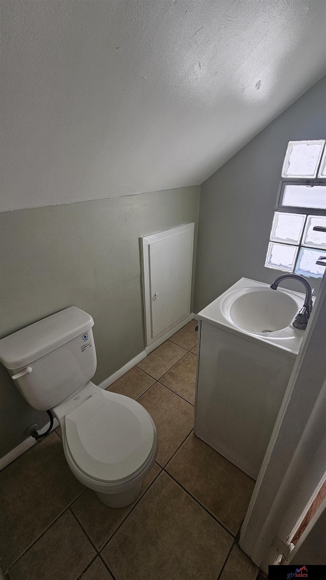 bathroom with tile patterned floors, toilet, sink, vaulted ceiling, and a textured ceiling