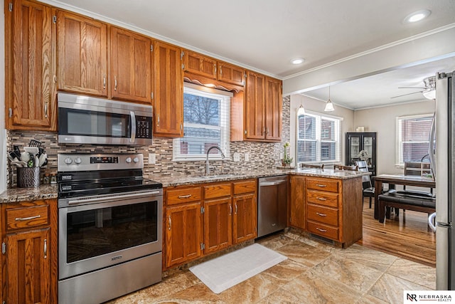 kitchen featuring a peninsula, appliances with stainless steel finishes, brown cabinetry, and a sink