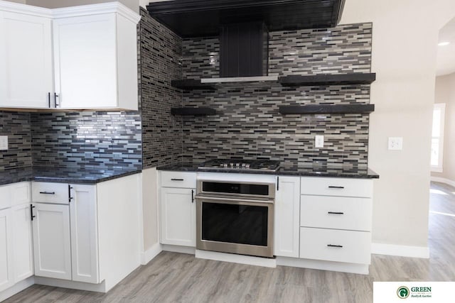 kitchen with white cabinetry, appliances with stainless steel finishes, range hood, and tasteful backsplash