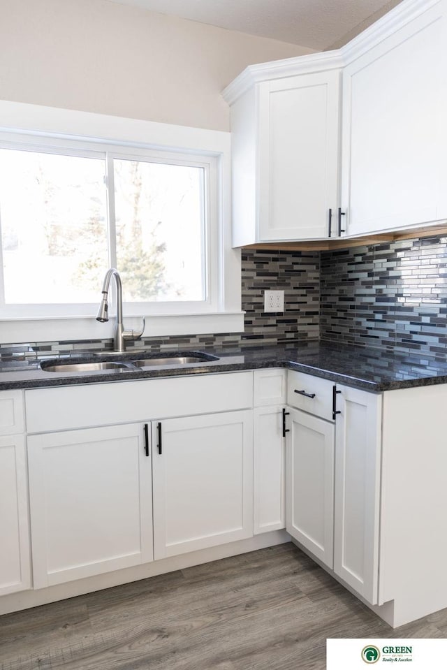 kitchen featuring hardwood / wood-style floors, sink, dark stone countertops, white cabinets, and backsplash