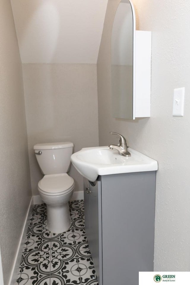 bathroom with tile patterned flooring, vanity, vaulted ceiling, and toilet