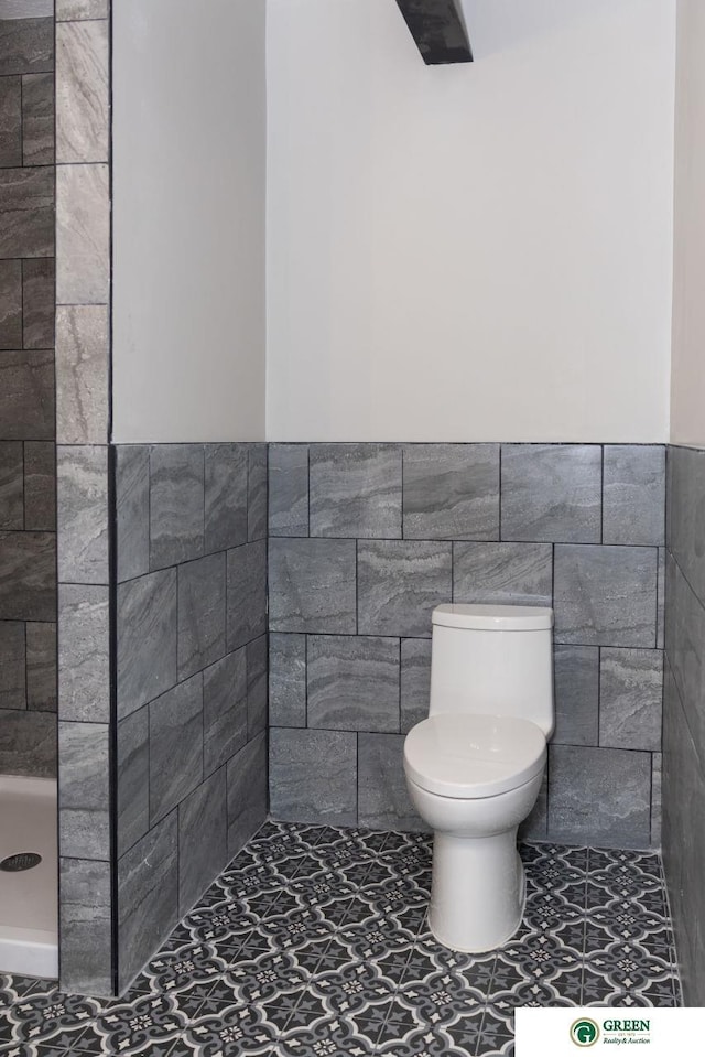 bathroom featuring a tile shower, tile walls, and toilet