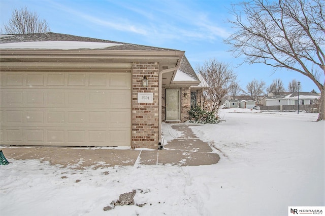 view of snow covered exterior with brick siding and roof with shingles