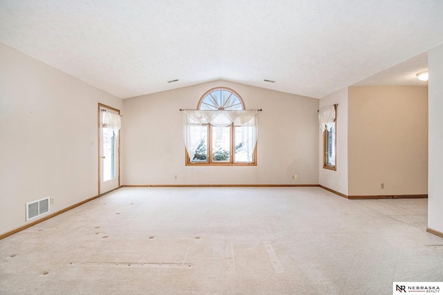 empty room featuring light colored carpet, visible vents, vaulted ceiling, and baseboards