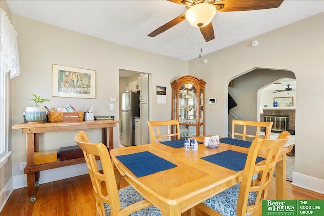 dining space with a brick fireplace, hardwood / wood-style flooring, a textured ceiling, and ceiling fan