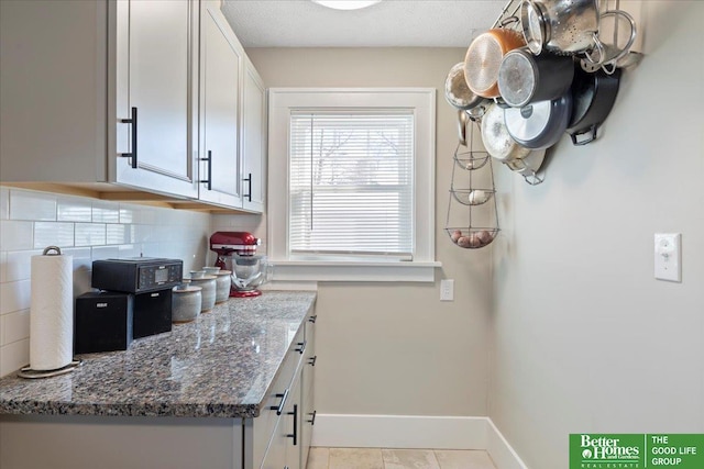 kitchen featuring light tile patterned floors, white cabinetry, backsplash, a textured ceiling, and dark stone counters