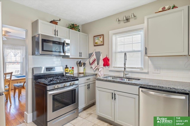 kitchen with sink, a textured ceiling, appliances with stainless steel finishes, white cabinets, and backsplash