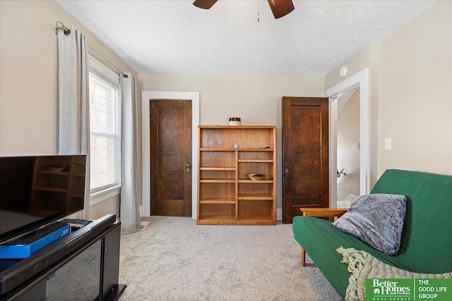 living area with ceiling fan, light colored carpet, and a textured ceiling