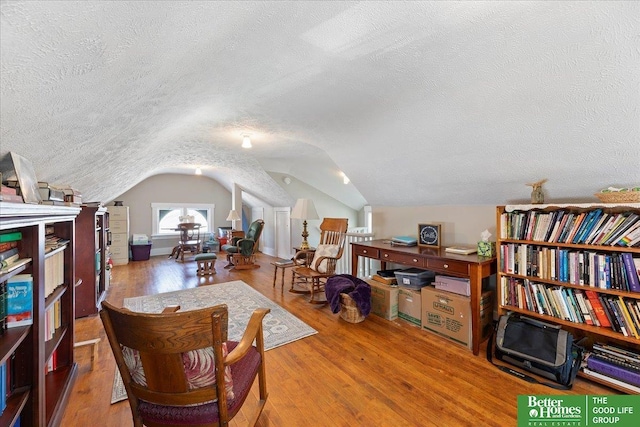 living area featuring vaulted ceiling, hardwood / wood-style floors, and a textured ceiling