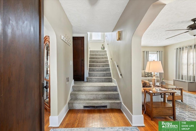 stairs featuring hardwood / wood-style floors, a textured ceiling, and ceiling fan