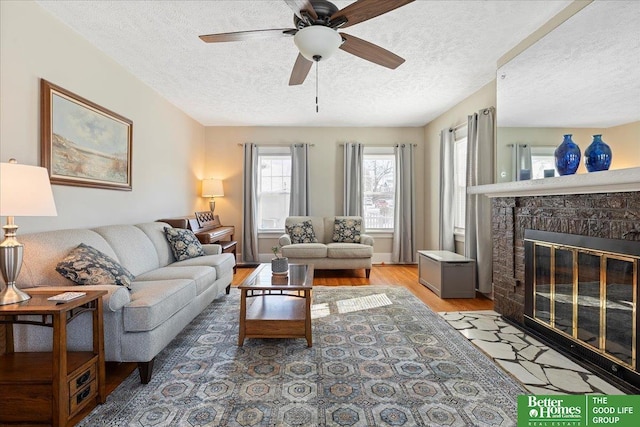 living room featuring ceiling fan, hardwood / wood-style flooring, a fireplace, and a textured ceiling