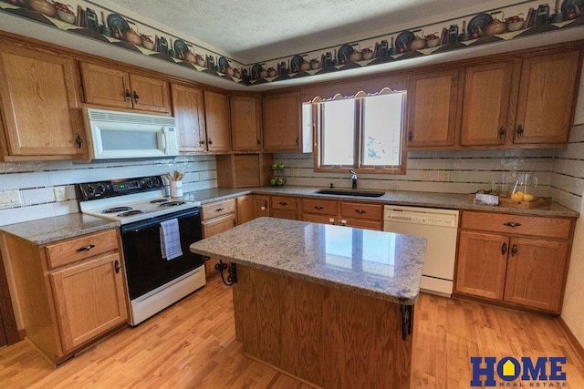 kitchen with sink, light stone counters, a center island, white appliances, and light hardwood / wood-style floors