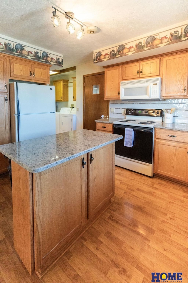 kitchen with light stone counters, white appliances, light wood-type flooring, a kitchen island, and independent washer and dryer