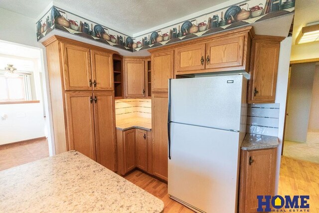 kitchen with light stone countertops, white fridge, a textured ceiling, and light hardwood / wood-style flooring