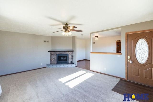 foyer entrance with a brick fireplace, dark carpet, and ceiling fan