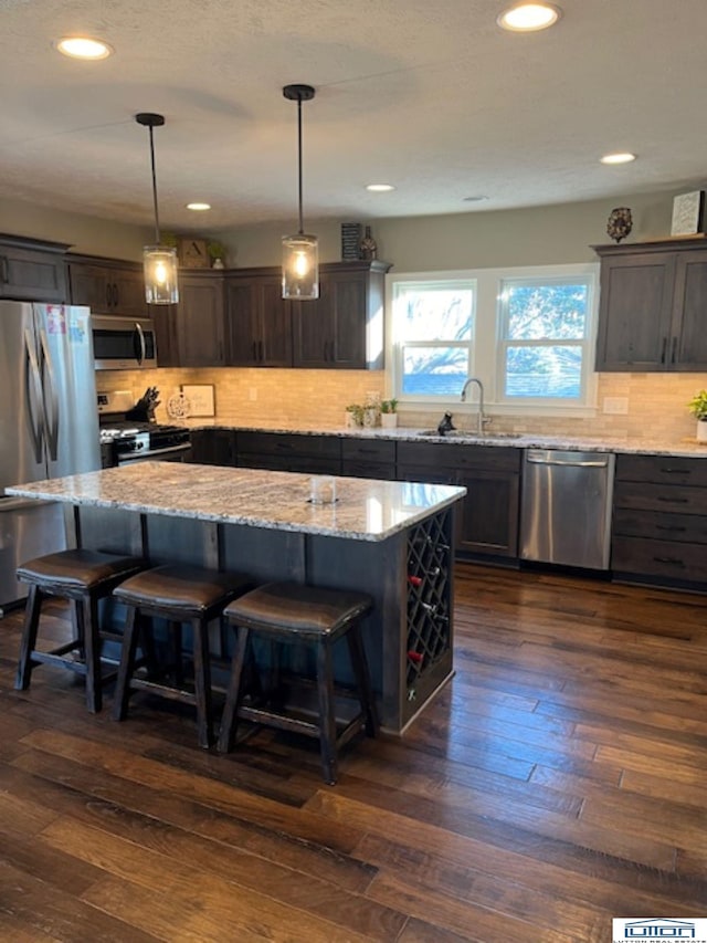 kitchen featuring sink, decorative light fixtures, dark brown cabinets, appliances with stainless steel finishes, and a kitchen island