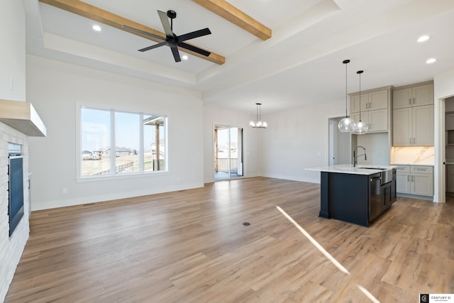 unfurnished living room featuring sink, a raised ceiling, light hardwood / wood-style floors, beamed ceiling, and ceiling fan with notable chandelier