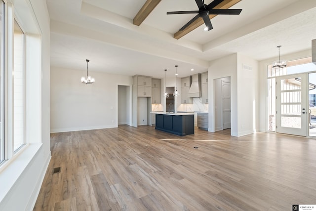 unfurnished living room with beam ceiling, sink, ceiling fan with notable chandelier, and light wood-type flooring