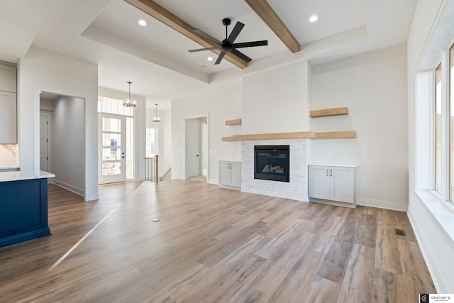 unfurnished living room with beam ceiling, light hardwood / wood-style flooring, a raised ceiling, and ceiling fan