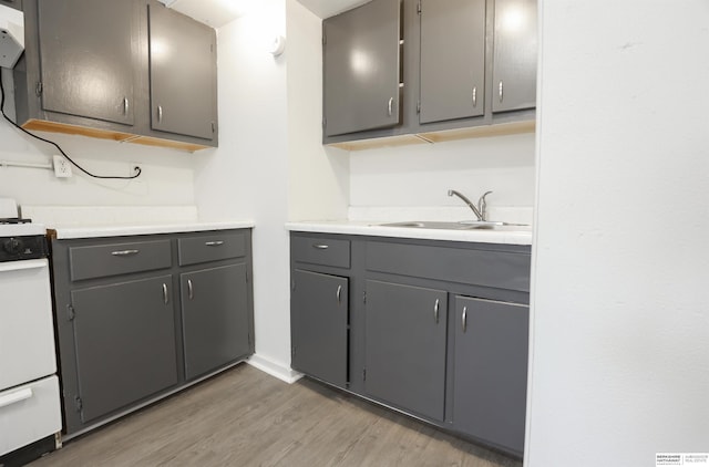 kitchen featuring white range, sink, gray cabinetry, and light hardwood / wood-style floors