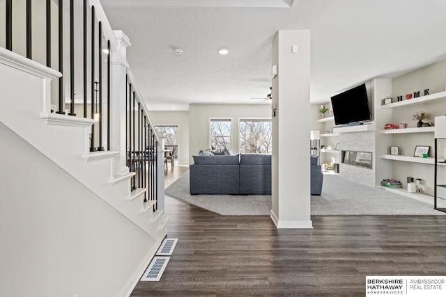 living room with ceiling fan, dark wood-type flooring, a fireplace, and built in shelves