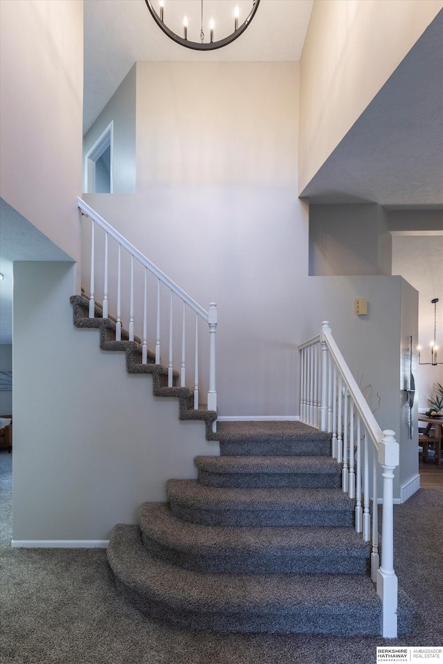 staircase with carpet flooring, a chandelier, and a towering ceiling