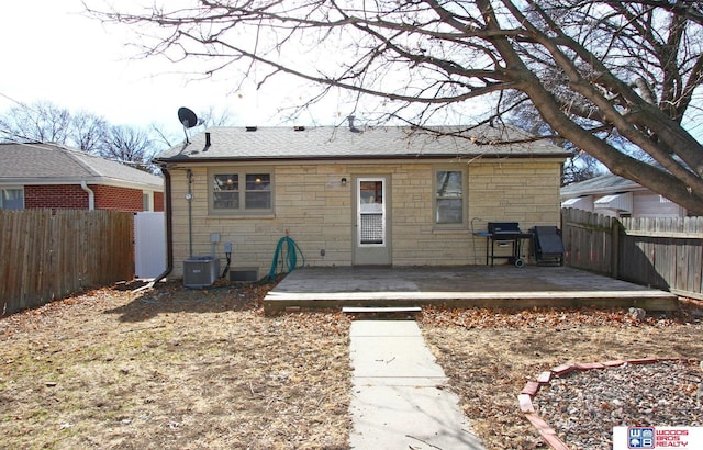 rear view of house with stone siding, central AC, a fenced backyard, and a wooden deck