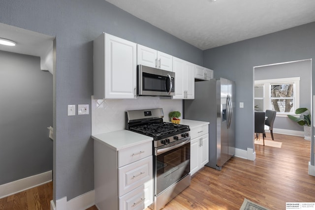 kitchen featuring appliances with stainless steel finishes, light wood-type flooring, white cabinets, decorative backsplash, and a textured ceiling