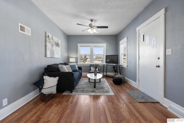 living room featuring a textured ceiling, dark wood-type flooring, and ceiling fan