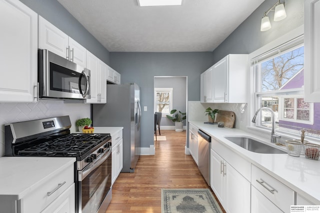 kitchen featuring sink, white cabinetry, light wood-type flooring, stainless steel appliances, and decorative backsplash