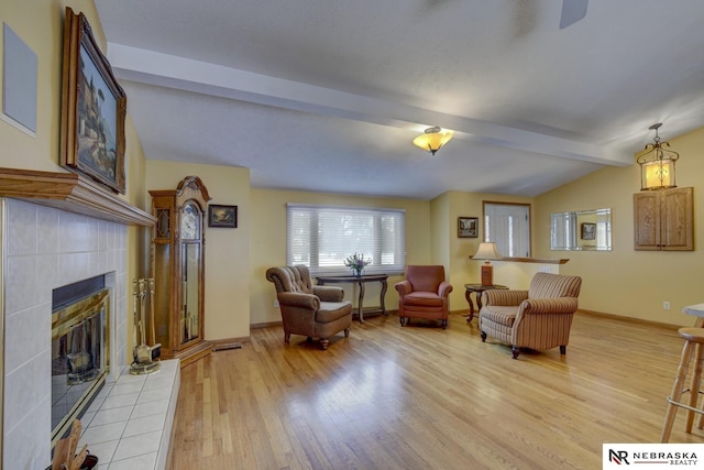 living room featuring light hardwood / wood-style floors, a tile fireplace, and vaulted ceiling with beams