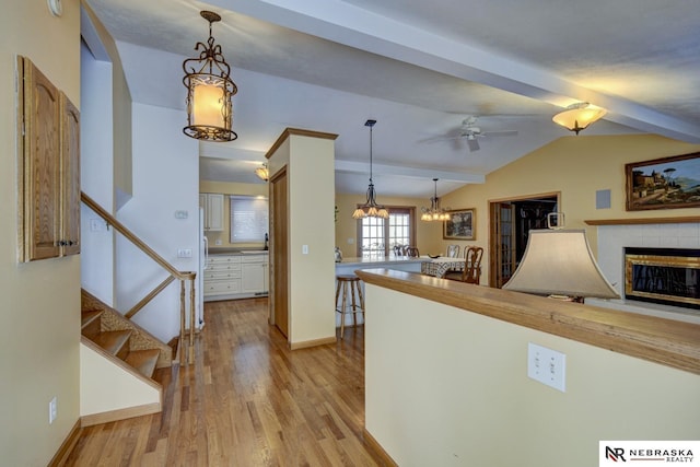 kitchen featuring vaulted ceiling with beams, pendant lighting, a fireplace, and light wood-type flooring