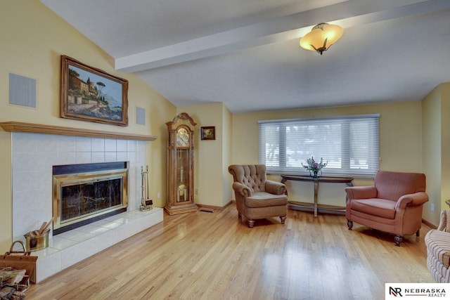 sitting room featuring a baseboard heating unit, a tile fireplace, vaulted ceiling with beams, and light hardwood / wood-style flooring