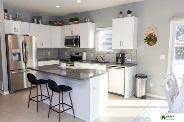 kitchen with appliances with stainless steel finishes, white cabinetry, sink, a kitchen breakfast bar, and a center island