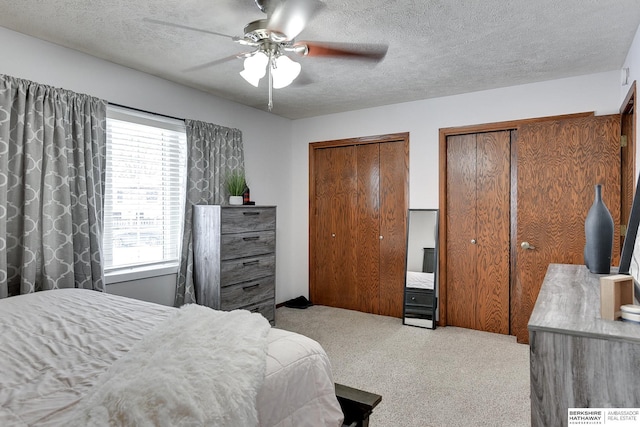 carpeted bedroom with ceiling fan, a textured ceiling, and multiple closets