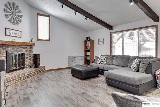 living room with a fireplace, lofted ceiling with beams, rail lighting, a textured ceiling, and light wood-type flooring