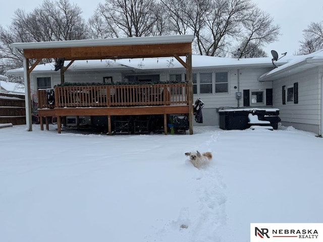 snow covered back of property with a wooden deck and a jacuzzi