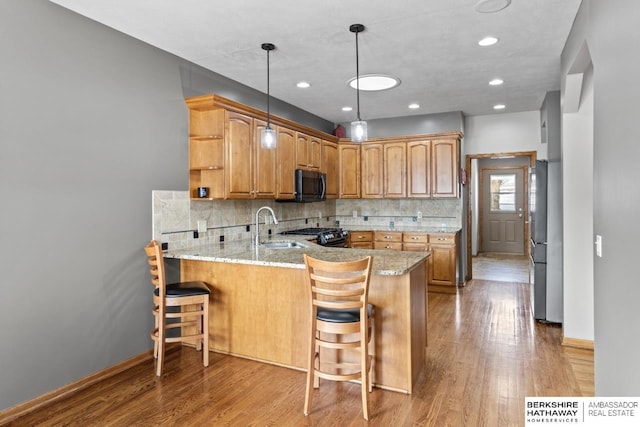 kitchen featuring sink, stainless steel refrigerator, light stone counters, a kitchen bar, and kitchen peninsula