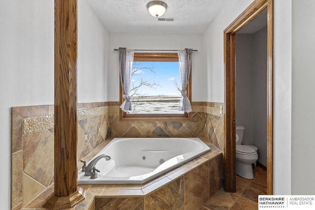 bathroom featuring tiled tub, a textured ceiling, and toilet