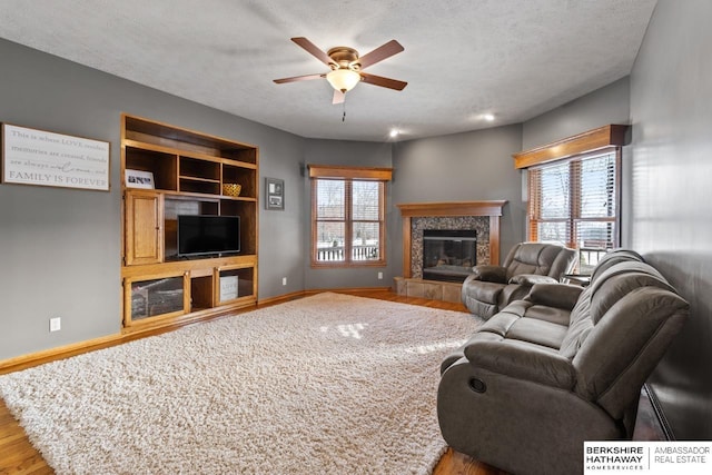 living room with a tiled fireplace, a textured ceiling, light hardwood / wood-style floors, and ceiling fan