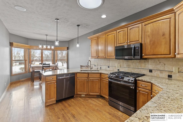 kitchen featuring sink, hanging light fixtures, stainless steel appliances, light stone counters, and kitchen peninsula