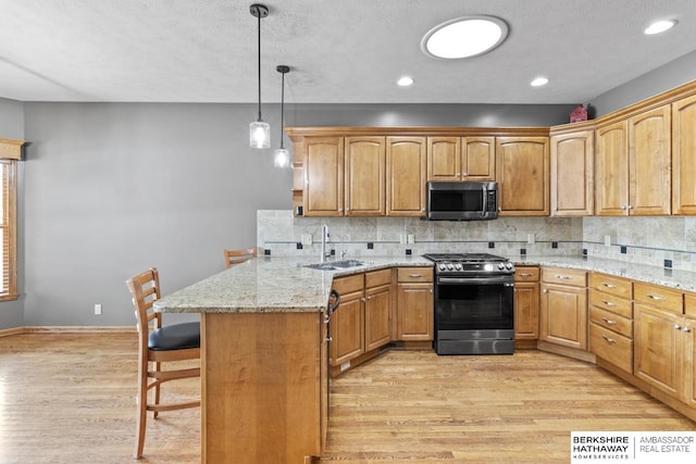 kitchen with sink, a breakfast bar area, hanging light fixtures, appliances with stainless steel finishes, and kitchen peninsula