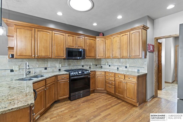 kitchen featuring decorative light fixtures, sink, light stone counters, stainless steel gas range oven, and light hardwood / wood-style flooring